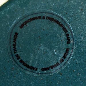 Pode incluir: Um close-up de um prato de cer&acirc;mica azul-esverdeado com um adesivo preto que diz "Microwave & Dishwasher Safe. Original Thailand. Fabulous in Thailand."