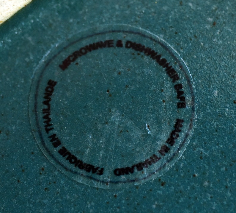 Pode incluir: Um close-up de um prato de cer&acirc;mica azul-esverdeado com um adesivo preto que diz "Microwave & Dishwasher Safe. Original Thailand. Fabulous in Thailand."
