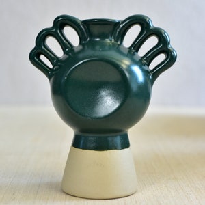Pode incluir: Um vaso de cer&acirc;mica verde escuro com um design &uacute;nico que apresenta m&uacute;ltiplas al&ccedil;as. O vaso tem uma base branca e um acabamento liso e brilhante.