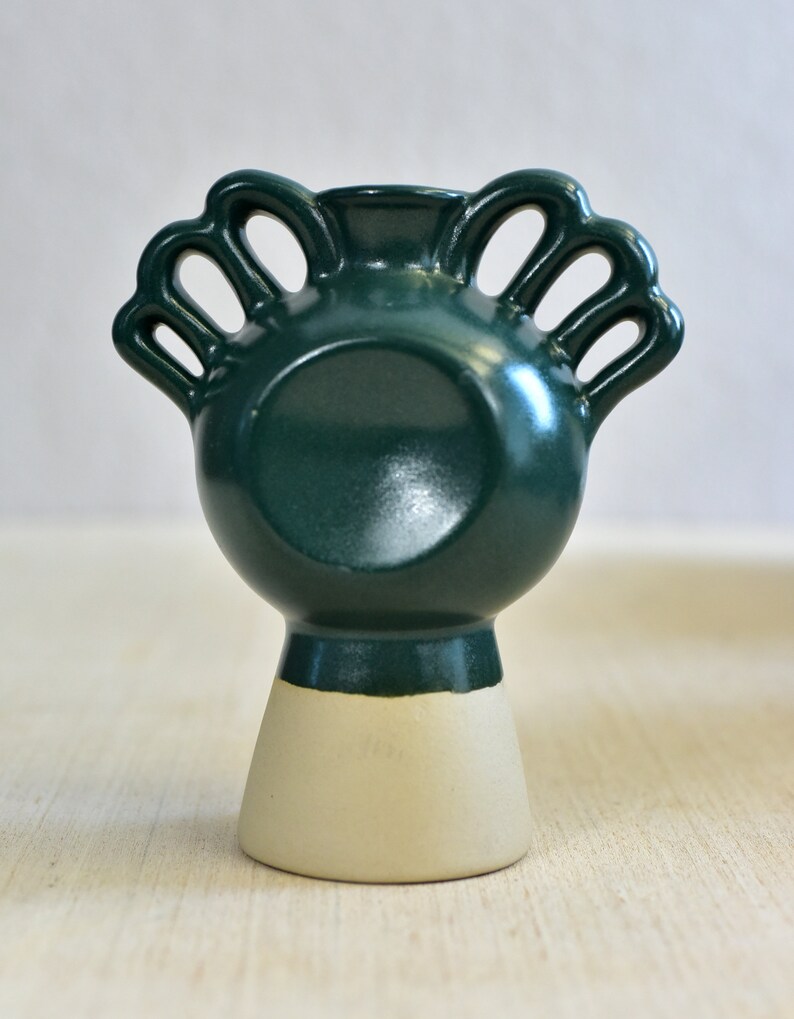 Pode incluir: Um vaso de cer&acirc;mica verde escuro com um design &uacute;nico que apresenta m&uacute;ltiplas al&ccedil;as. O vaso tem uma base branca e um acabamento liso e brilhante.
