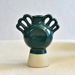 Pode incluir: Um vaso de cer&acirc;mica verde escuro com corpo redondo e base branca. O vaso tem quatro al&ccedil;as em forma de la&ccedil;os.