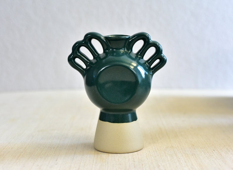 Pode incluir: Um vaso de cer&acirc;mica verde escuro com corpo redondo e base branca. O vaso tem quatro al&ccedil;as em forma de la&ccedil;os.