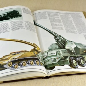 May include: An open book with illustrations of two military vehicles. The book is titled "255 and DANA". The first vehicle is a green self-propelled howitzer with a long barrel and six wheels. The second vehicle is a tan self-propelled howitzer with a long barrel and tracks.