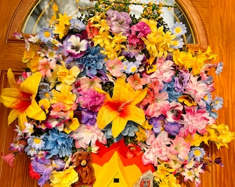May include: A colorful floral wreath with a yellow, red, and orange painted wooden sign that says "must ride alone". The sign is shaped like a tent with a bear and a red rock.