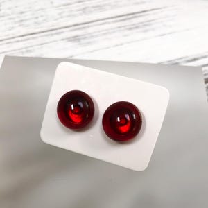 May include: A pair of red glass stud earrings. The earrings are round and have a slightly raised centre.