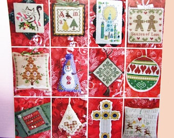 May include: A collection of cross-stitch Christmas ornaments. Designs include a cat with a candy cane, a pear and tree, a snowman, gingerbread men, a Christmas tree, a cross, and a Christmas ball. The ornaments are on a red background.