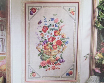 May include: A cross-stitch embroidery of a floral arrangement in a gold urn. The flowers are red, pink, white, and blue, and the urn is surrounded by green leaves and fruit.
