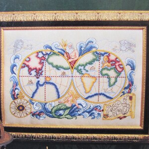 May include: Cross-stitch world map framed in gold. The map features two hemispheres with continents in red, green, and yellow, surrounded by blue waves, a mermaid, and a trident-wielding figure. The frame is rectangular with ornate detailing.
