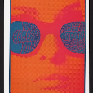 May include: A retro-style poster featuring a face with orange and red hues. The eyes are replaced by blue sunglasses with the text "THE MONKEES BIRDS" and other text. The poster has a vintage, psychedelic aesthetic.
