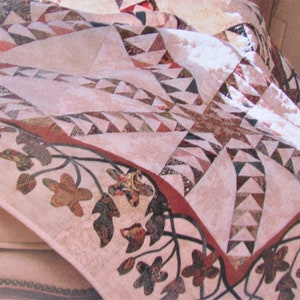 Peut inclure: Une courtepointe avec un motif de patchwork rose et brun. La courtepointe a une bordure de vignes brunes avec des feuilles et des fleurs.