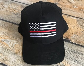 May include: Black baseball cap with an embroidered American flag featuring a red stripe across the middle.