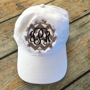 May include: White baseball cap with a distressed, round patch featuring a gray and white chevron pattern and black embroidered initials "EPR".