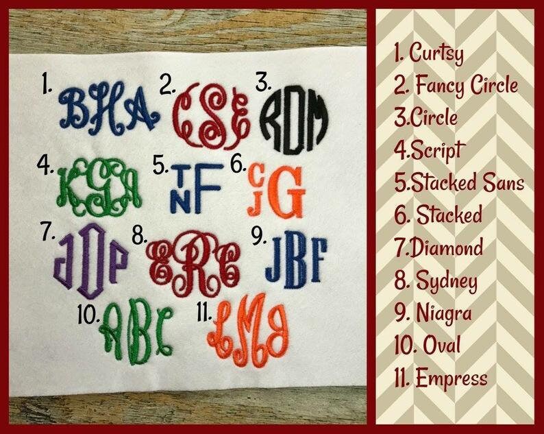 May include: A white fabric swatch with 11 different embroidered monogram styles numbered 1 through 11. Each monogram is a different colour and font style. The text "Curtsy, Fancy Circle, Circle, Script, Stacked Sans, Stacked, Diamond, Sydney, Niagra, Oval, Empress" is listed on the right side of the image.