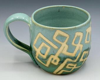 Wheel-thrown mug with wax patterns and soft blue and patina green glazes