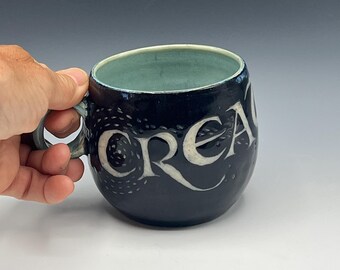 Wheel-thrown mug with hand-carved design "create" and soft blue interior glaze