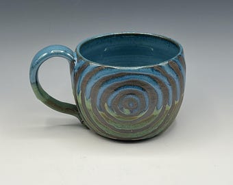 Wheel-thrown mug with wax resist spiral enhanced with blue and patina green glaze