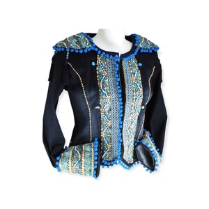 Könnte beinhalten: Eine dunkelblaue Jeansjacke mit goldenen und blauen Stickereien und Bommeln an den Rändern.