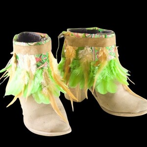 May include: A pair of beige suede ankle boots with green and brown feather trim. The boots have a pointed toe and a low heel.