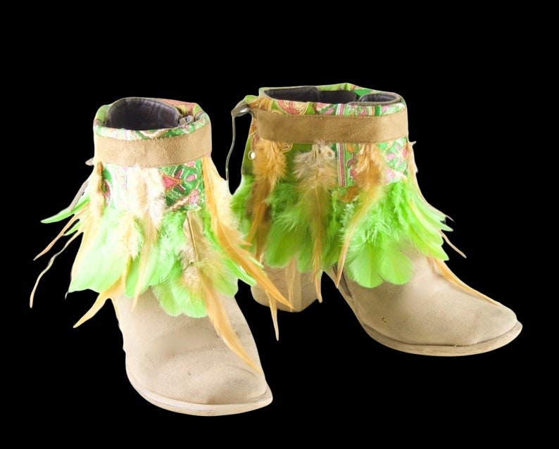 May include: A pair of beige suede ankle boots with green and brown feather trim. The boots have a pointed toe and a low heel.