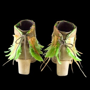 May include: A pair of brown suede ankle boots with green and beige feather trim. The boots have a chunky heel and a lace-up closure.