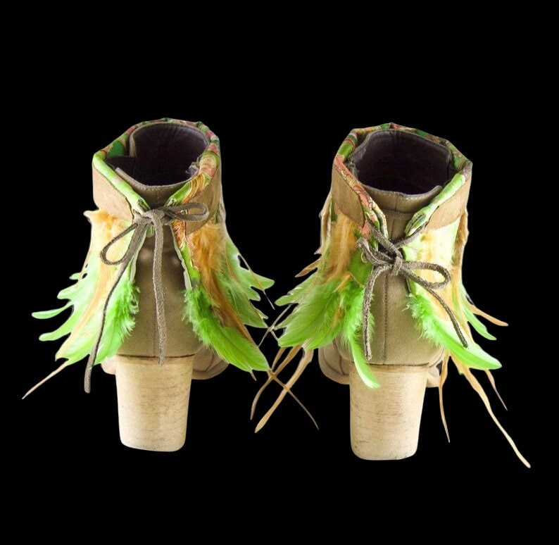 May include: A pair of brown suede ankle boots with green and beige feather trim. The boots have a chunky heel and a lace-up closure.