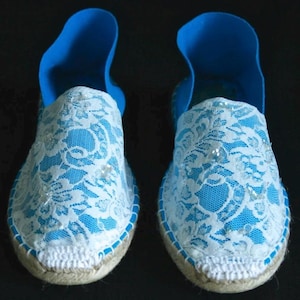 May include: A pair of blue espadrille shoes with white lace and pearl embellishments.
