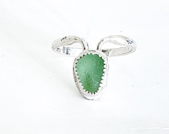 Op de afbeelding: Een zilveren ring met een groene steen in het midden. De ring heeft een uniek ontwerp met twee banden die om de vinger wikkelen.