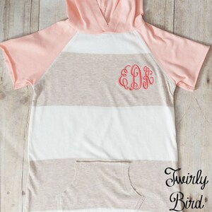 May include: A striped hooded shirt with a peach colored hood and sleeves. The shirt has a pocket on the front and the letters "EDK" embroidered on the chest. The shirt is made by "Twirly Bird Design."
