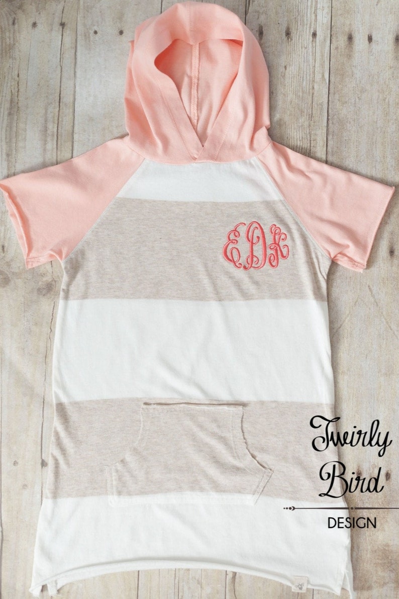 May include: A striped hooded shirt with a peach colored hood and sleeves. The shirt has a pocket on the front and the letters "EDK" embroidered on the chest. The shirt is made by "Twirly Bird Design."