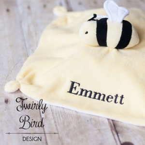 Puede incluir: Una manta de seguridad para bebé en forma de abeja amarilla y negra con el nombre "Emmett" bordado. La manta está hecha por "Twirly Bird Design".