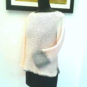 Può includere: Un maglione di maglia di colore rosa chiaro con una manica grigia. Il maglione è su un manichino nero.