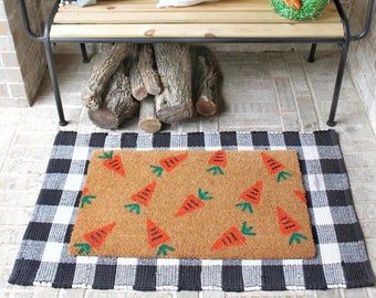 May include: A black and white checkered doormat with a brown coir insert featuring a pattern of orange carrots.