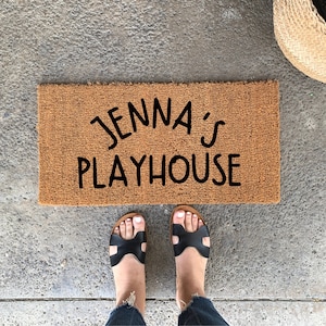 May include: A brown coir doormat with the text "Jenna's Playhouse" in black lettering.
