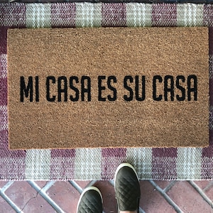 May include: A brown coir doormat with the text "MI CASA ES SU CASA" in black lettering.