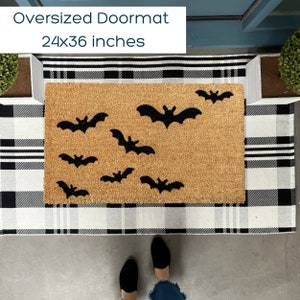 May include: Oversized doormat with a Halloween theme. The doormat is brown and features black bats. The doormat is 24x36 inches.