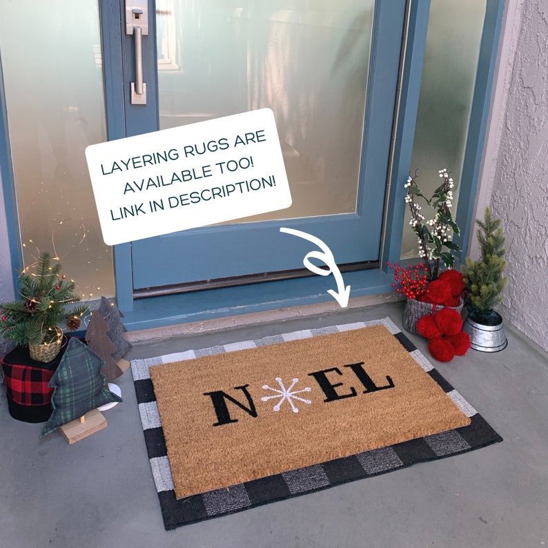 May include: A brown coir doormat with a black and white checkered border. The doormat has the word "NOEL" written in black with a white snowflake in between the "N" and "E".