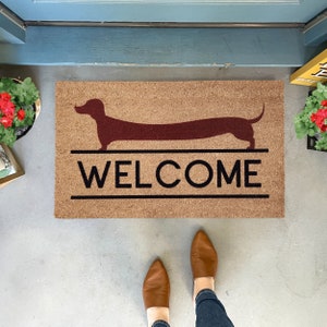 May include: A brown coir doormat with a red dachshund silhouette and the word "WELCOME" in black lettering.