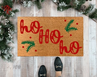 May include: A brown coir doormat with the text "ho ho ho" in red lettering and green pine sprigs.