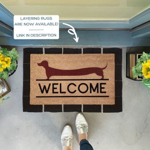 May include: A brown coir welcome mat with black trim features a red dachshund silhouette and the word "WELCOME" in black lettering.