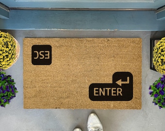 May include: A brown coir doormat with the words "ESC" and "ENTER" printed in black. The word "ENTER" is printed on a black key icon with a left arrow.