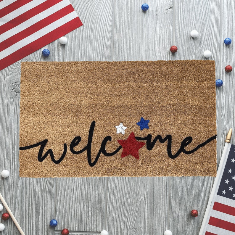 May include: A brown welcome mat with the word "welcome" in black script. The word is decorated with red, white, and blue stars.