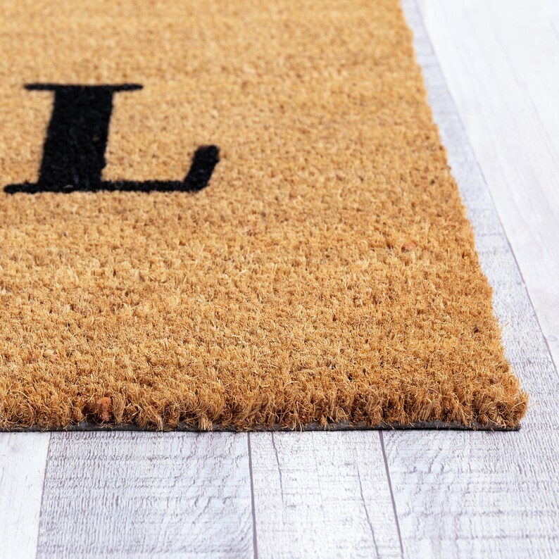 May include: A brown coir doormat with the letter "L" printed in black.