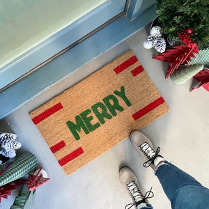 May include: A brown coir doormat with red stripes and the word "Merry" in green lettering.