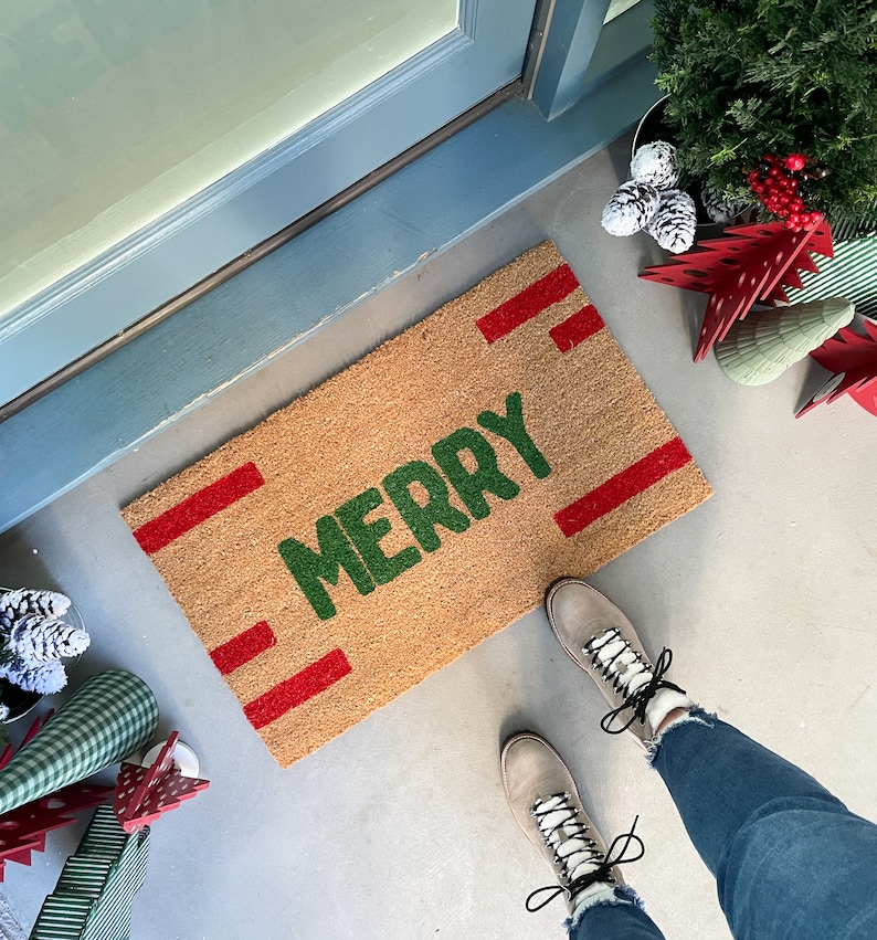May include: A brown coir doormat with red stripes and the word "Merry" in green lettering.