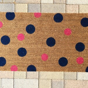 May include: A brown coir doormat with a polka dot pattern. The dots are in shades of pink and blue.