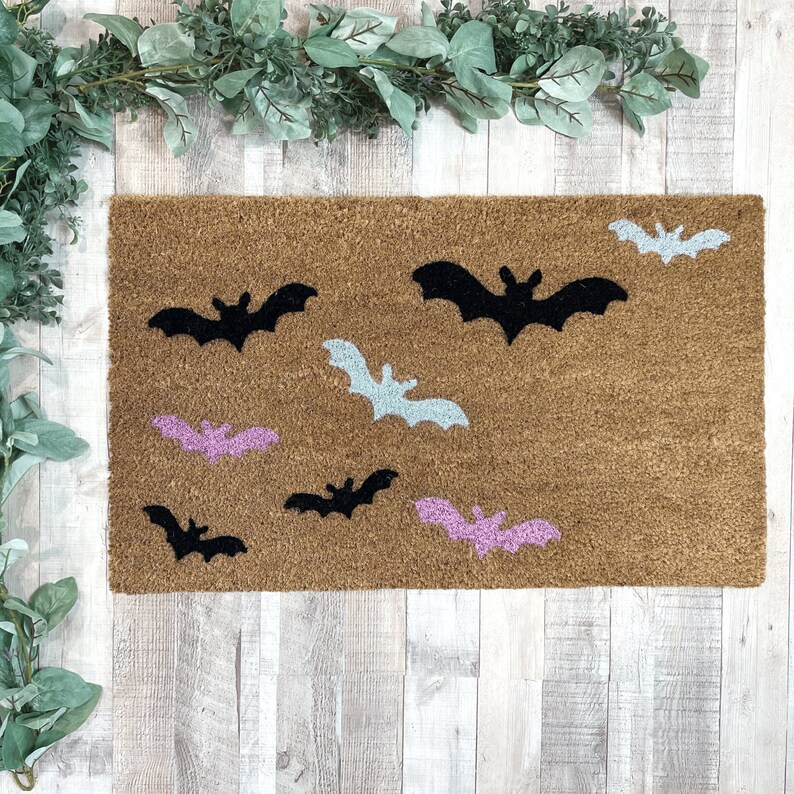 May include: A brown doormat with a variety of black, pink, and light blue bats. The bats are in different sizes and positions.
