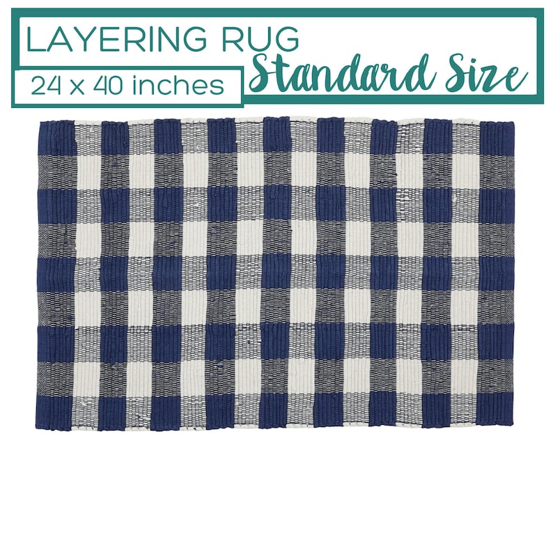May include: A rectangular layering rug with a blue and white checkered pattern. The rug measures 24 x 40 inches and is labeled "Standard Size". The text "Layering Rug" is at the top.