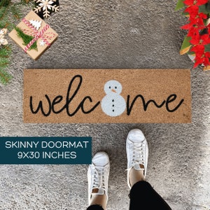May include: A brown coir doormat with the word "welcome" in black script and a white snowman in the center. The doormat is 9 inches by 30 inches.