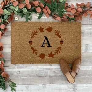 May include: A brown coir doormat with the letter "A" in a wreath of brown leaves and acorns.