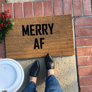 May include: A brown doormat with the text "Merry AF" in black lettering.